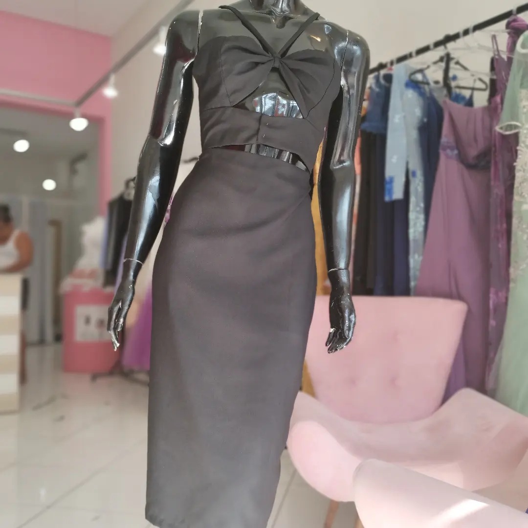 Vestido midi preto sob medida no manequim, com araras e poltrona rosa ao fundo