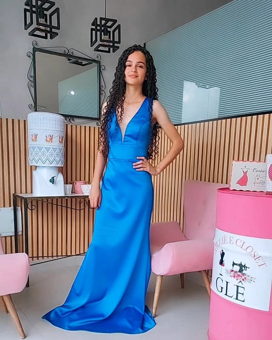 Cliente com vestido longo azul em cetim, ao lado das poltronas rosa e do tonel com a logo do ateliê