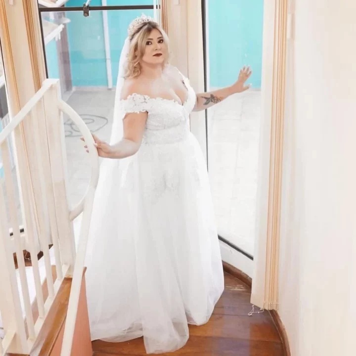 Noiva vestida pelo ateliê, de vestido branco com renda e véu, em uma escada